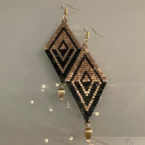 Peut inclure: Une paire de boucles d'oreilles pendantes géométriques noires et dorées en forme de diamant avec une petite perle dorée au bas de chaque boucle d'oreille.