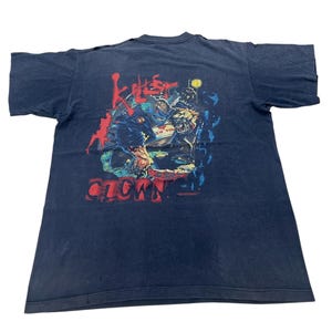 Op de afbeelding: Donkerblauwe t-shirt met een afbeelding van een clown en de tekst "Killer Clown" in het rood. Het ontwerp bevat een stadsgezicht en andere figuren. Dit is een vintage item.