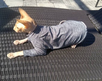 May include: A hairless cat wearing a gray and white striped long-sleeved shirt, lying on a black wicker surface.