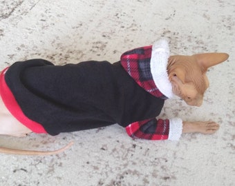 May include: A black hooded sweater with red and black plaid trim, worn by a hairless cat. The sweater has a white fleece lining around the hood and cuffs.