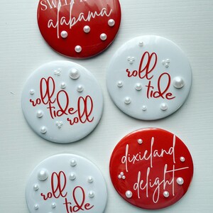 May include: Set of five round coasters. Two red coasters feature the phrases "Sweet Home Alabama" and "Dixieland Delight" in white script. Three white coasters have the phrase "roll tide" in red script. Each coaster is decorated with faux pearls.