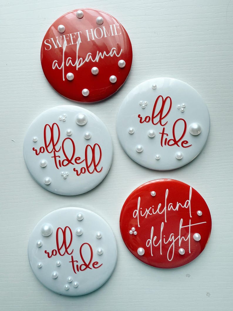 May include: Set of five round coasters. Two red coasters feature the phrases "Sweet Home Alabama" and "Dixieland Delight" in white script. Three white coasters have the phrase "roll tide" in red script. Each coaster is decorated with faux pearls.