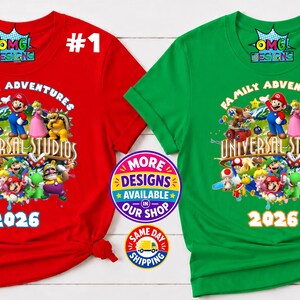 May include: A red and a green short-sleeved t-shirt, each featuring a graphic print of various video game characters, the text "FAMILY ADVENTURES UNIVERSAL STUDIOS" and "2026". The shirts include a small "OMG DESIGNS" logo at the top center.