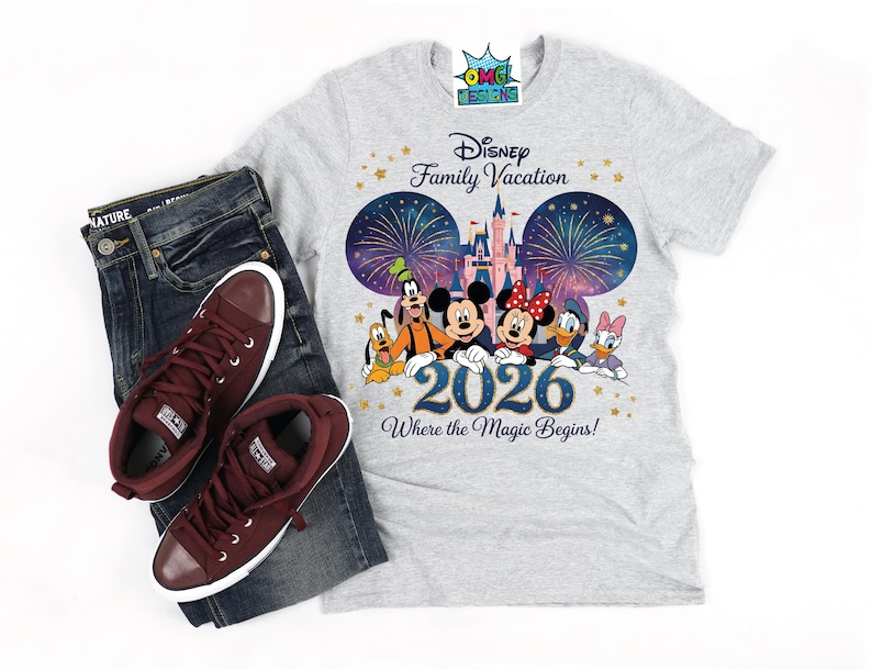 Puede incluir: Una camiseta gris claro con un gr&aacute;fico de Disney Family Vacation 2026 con Mickey Mouse, Minnie Mouse, Goofy, Pluto, Donald Duck y Daisy Duck frente a un castillo con fuegos artificiales. El texto dice Disney Family Vacation 2026 Where the Magic Begins.