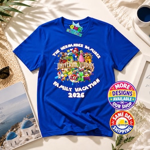 May include: A royal blue short-sleeve t-shirt featuring a graphic print of various Super Mario characters surrounding the text Universal Studios. The shirt includes the custom text The Hernandez Ramirez Family Vacation 2026 printed in white.
