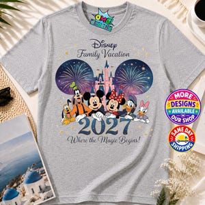 Puede incluir: Una camiseta gris jaspeado con un gr&aacute;fico de personajes de Disney que incluye a Mickey, Minnie, Goofy, Pluto, Donald y Daisy frente a un castillo y fuegos artificiales. El texto dice Disney Family Vacation 2027 Where the Magic Begins.