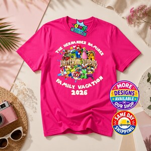 May include: A bright pink short-sleeved t-shirt featuring a graphic print of various Nintendo characters, the text THE HERNANDEZ RAMIREZ UNIVERSAL STUDIOS FAMILY VACATION 2026, and a small logo at the top that reads OMG DESIGNS.