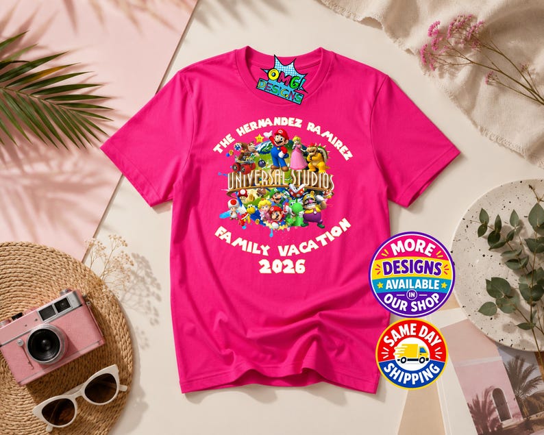 May include: A bright pink short-sleeved t-shirt featuring a graphic print of various Nintendo characters, the text THE HERNANDEZ RAMIREZ UNIVERSAL STUDIOS FAMILY VACATION 2026, and a small logo at the top that reads OMG DESIGNS.