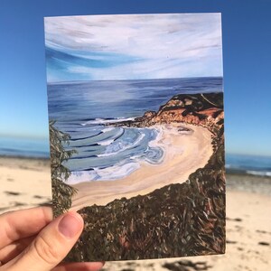 Puede incluir: Una postal con una pintura de una escena de playa con agua azul, arena blanca y vegetación verde. La pintura está enmarcada por un borde blanco.
