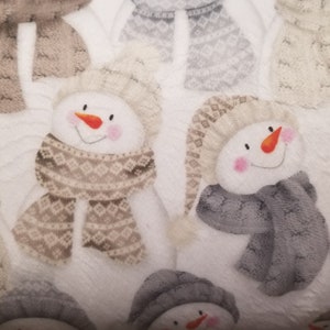 May include: White fabric with a repeating pattern of snowmen wearing knit hats and scarves. The snowmen have rosy cheeks and orange noses. The scarves are in shades of brown and gray.