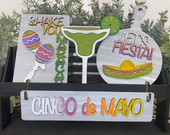 May include: Wooden signs with a Cinco de Mayo theme. The signs feature phrases like "Shake Your Maracas", "Let's Fiesta!" and "Cinco de Mayo". The signs are decorated with colorful maracas, a sombrero, and a margarita glass.
