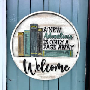 May include: A round wooden sign with a white background and a distressed finish. The sign features a stack of books with the text "A NEW Adventure IS ONLY A PAGE AWAY" and the word "Welcome" in black lettering.