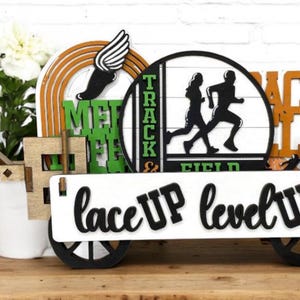 May include: A wooden wagon with a white sign that says "lace up level up". The wagon is decorated with various signs, including "Track & Field", "Meet", and "Back Hill".