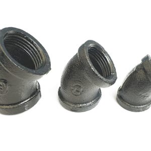 May include: Three black iron pipe fittings, each with a 45-degree angle, are arranged in a row from largest to smallest.