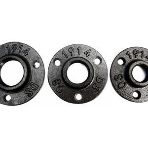 May include: Three black metal pipe flanges with a 1 1/2 inch inner diameter and three bolt holes. The flanges are marked with the number "1914" and the letters "DSS".