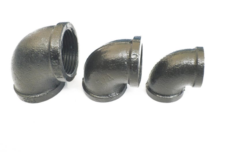 May include: Three black iron pipe fittings, each with a 90-degree angle, are shown on a white background. The fittings are threaded on one end and have a smooth, black finish.