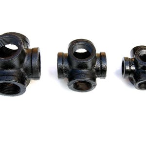 May include: Three black metal pipe fittings with six openings each. The fittings are different sizes.