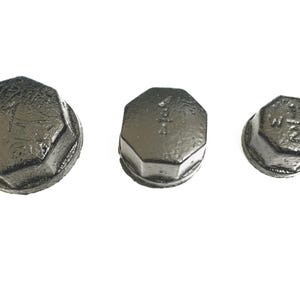 May include: Three black metal pipe caps of different sizes. The caps are hexagonal in shape and have a smooth, slightly textured surface. The largest cap has the text "1 1/2" inscribed on it, the middle cap has the text "1" inscribed on it, and the smallest cap has the text "1/2" inscribed on it.