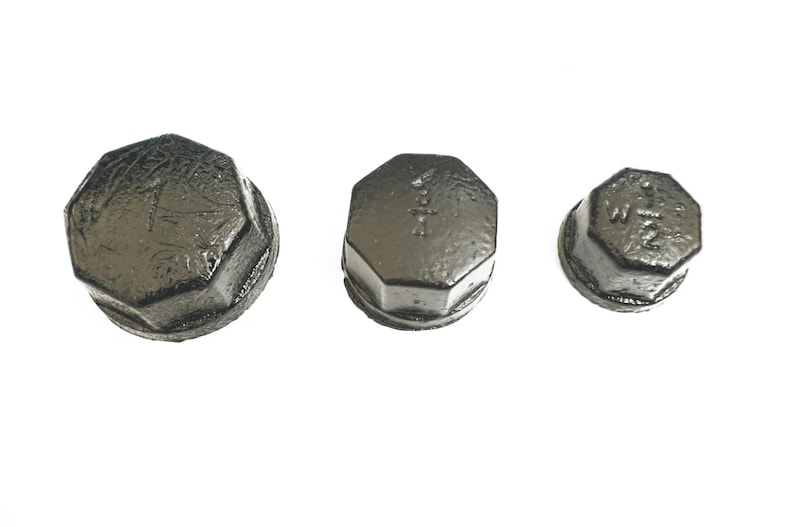 May include: Three black metal pipe caps of different sizes. The caps are hexagonal in shape and have a smooth, slightly textured surface. The largest cap has the text "1 1/2" inscribed on it, the middle cap has the text "1" inscribed on it, and the smallest cap has the text "1/2" inscribed on it.
