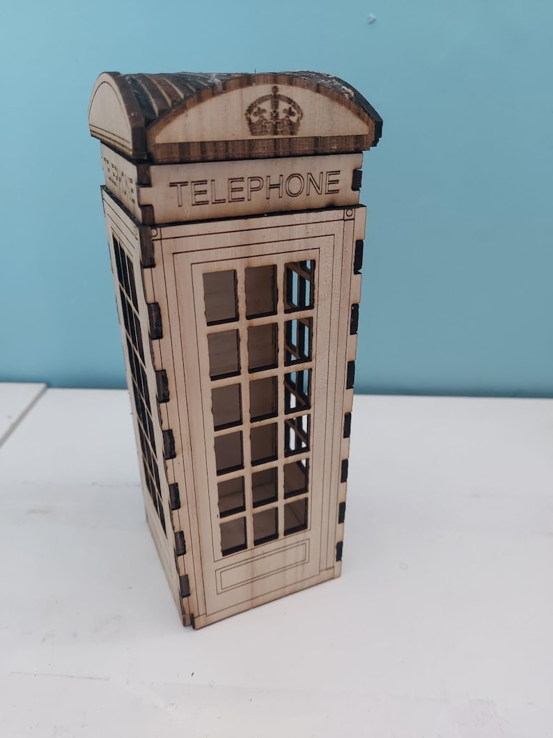 May include: A wooden model of a classic red British telephone booth with a crown on top and the word "TELEPHONE" printed on the front.
