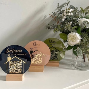 May include: Three round welcome signs with QR codes and the text "Scan for Wifi" on two of the signs and "Welcome to the O'Rourke's" on the other sign. The signs are on wooden stands and are in front of a white wall.