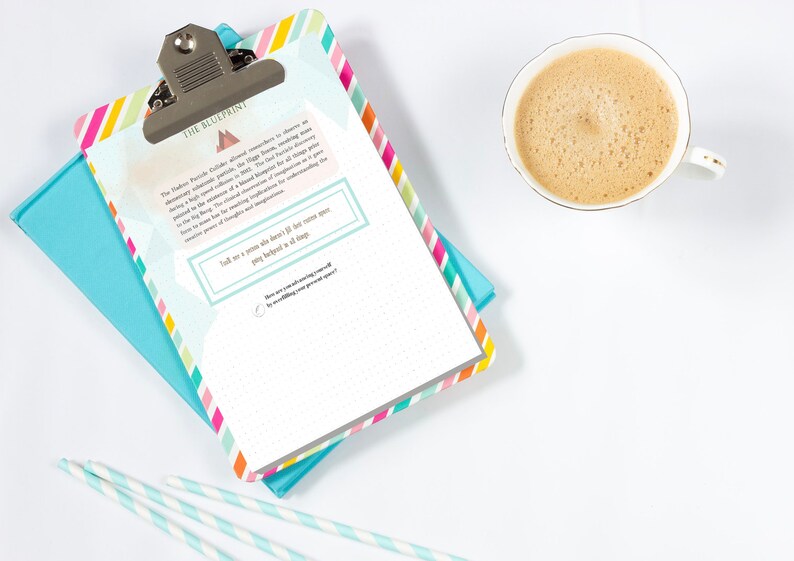 May include: A clipboard with a colorful striped border and a silver clip, resting on a teal notebook. The clipboard has text that reads "THE BLUEPRINT". A cup of coffee and striped straws are also in the image.