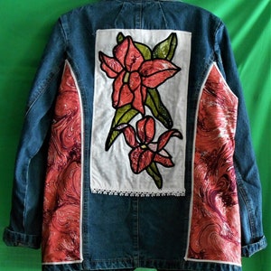 May include: A blue denim jacket with red and white fabric panels on the sides. The back of the jacket features a white panel with a red embroidered floral design.