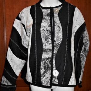 May include: Black and white quilted jacket with a marbled pattern and silver buttons. The jacket has a stand-up collar and long sleeves.