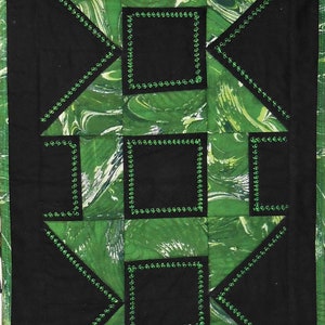 Op de afbeelding: Een groen en zwart quilt met een geometrisch patroon. De quilt is gemaakt van vierkanten en driehoeken, en de vierkanten zijn omlijnd met groen. De quilt is gemaakt van een stof met een marmerpatroon.