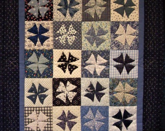 Puede incluir: Una colcha azul y blanca con un patrón de molinetes. La colcha está hecha de cuadrados con diferentes tonos de azul y blanco. La colcha está enmarcada con un borde azul oscuro.