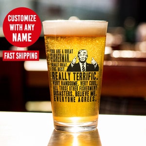 May include: A clear glass beer stein with a black and white graphic of a man with a thumbs up gesture. The graphic includes the text "You are a great fisherman. Really great. The best. Really terrific. Very handsome. Very cool. All those other fishermen? Disasters. Believe me. Everyone agrees."