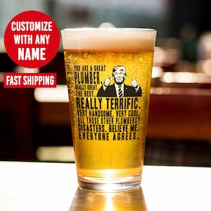 May include: A clear glass beer mug with a black and white graphic of a man with a thumbs up gesture. The text on the mug reads "You are a great plumber. Really great. The best. Really terrific. Very handsome. Very cool. All those other plumbers? Disasters. Believe me. Everyone agrees."