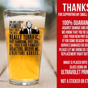 May include: A pint glass with a humorous image of a man with the text "You are a great plumber. Really great. The best. Really terrific. Very handsome. Very cool. All those other plumbers? Disasters. Believe me. Everyone agrees."