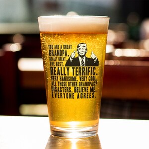 May include: A clear glass pint glass with a black and white graphic of a man with a thumbs up gesture. The text on the glass reads "You are a great Grandpa. Really great. The best. Really terrific. Very handsome. Very cool. All those other Grandpas? Disasters. Believe me. Everyone agrees."