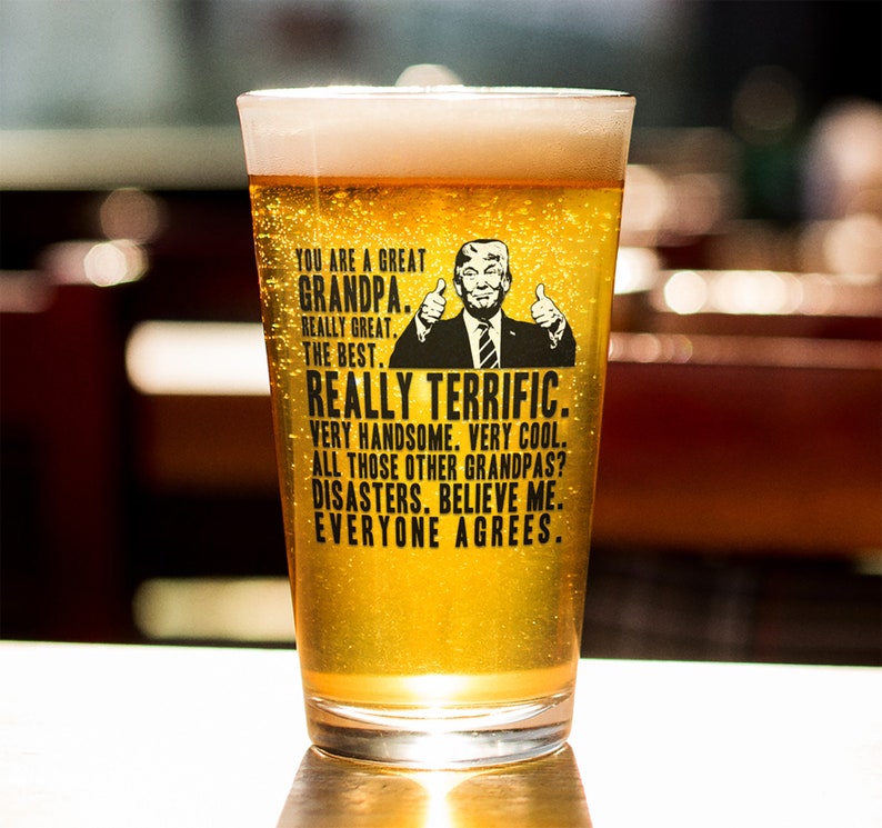 May include: A clear glass pint glass with a black and white graphic of a man with a thumbs up gesture. The text on the glass reads "You are a great Grandpa. Really great. The best. Really terrific. Very handsome. Very cool. All those other Grandpas? Disasters. Believe me. Everyone agrees."