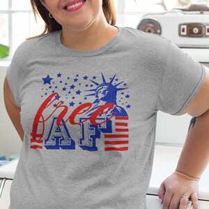 Peut inclure: T-shirt gris avec un motif graphique rouge, blanc et bleu repr&eacute;sentant la Statue de la Libert&eacute; et le texte "free AF".