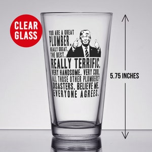 May include: A clear glass pint glass with a black and white image of a man with the text "You are a great plumber. Really great. The best. Really terrific. Very handsome. Very cool. All those other plumbers? Disasters. Believe me. Everyone agrees."