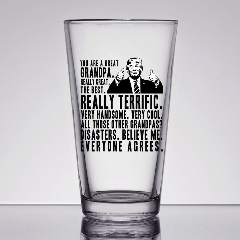 May include: A clear glass pint glass with a black and white image of a man with a thumbs up gesture and the text "You are a great Grandpa. Really great. The best. Really terrific. Very handsome. Very cool. All those other Grandpas? Disasters. Believe me. Everyone agrees."