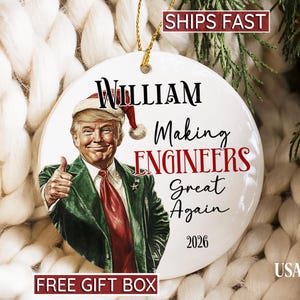 May include: A round white ceramic ornament featuring a graphic of a man in a Santa hat and green suit giving a thumbs up. The text reads William, Making ENGINEERS Great Again, and 2026. It includes a gold hanging string at the top.