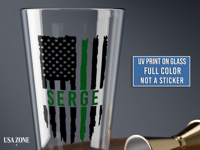 May include: A clear glass pint glass featuring a black and green distressed American flag graphic with the name SERGE printed in green. A blue rectangular box contains the text UV PRINT ON GLASS FULL COLOR NOT A STICKER.
