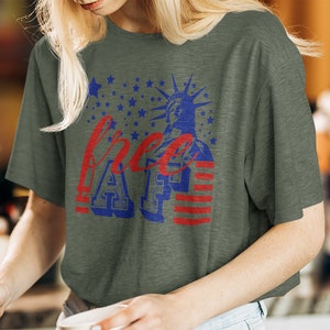 Peut inclure: Un t-shirt vert avec un motif graphique rouge, blanc et bleu. Le graphique repr&eacute;sente la Statue de la Libert&eacute;, des &eacute;toiles, des rayures et le texte "free AF".