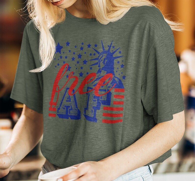 Peut inclure: Un t-shirt vert avec un motif graphique rouge, blanc et bleu. Le graphique repr&eacute;sente la Statue de la Libert&eacute;, des &eacute;toiles, des rayures et le texte "free AF".