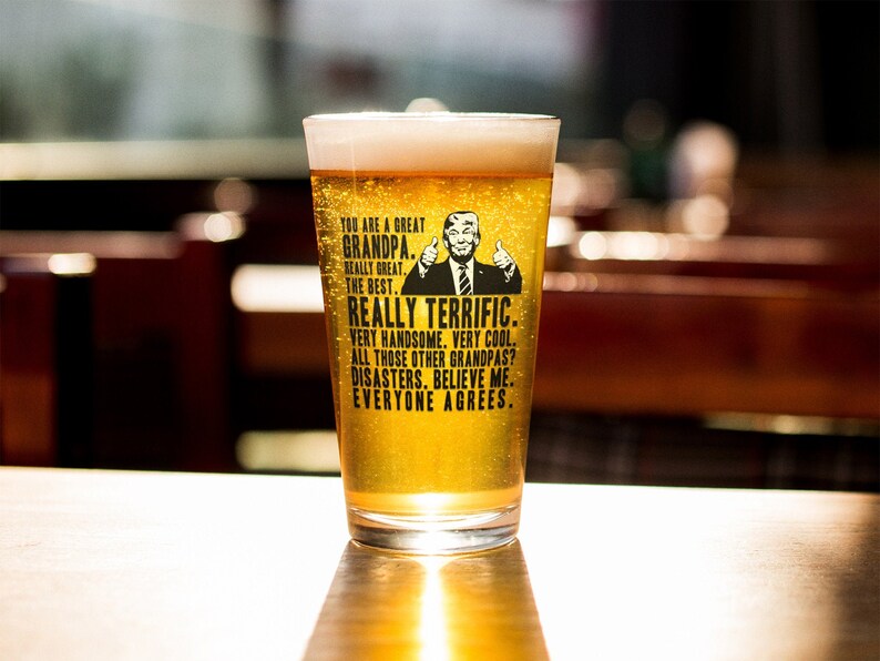 May include: A clear glass beer mug with a black and white image of a man with a thumbs up. The text on the mug reads "You are a great Grandpa. Really great. The best. Really terrific. Very handsome. Very cool. All those other Grandpas? Disasters. Believe me. Everyone agrees."