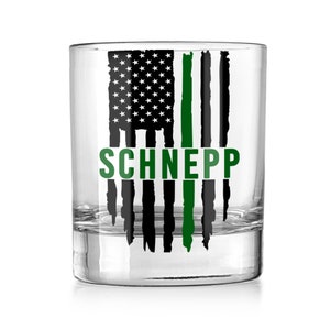 May include: A clear glass tumbler with a black and green American flag design. The flag has a thin green line down the center. The name "SCHNEPP" is printed in green below the flag.