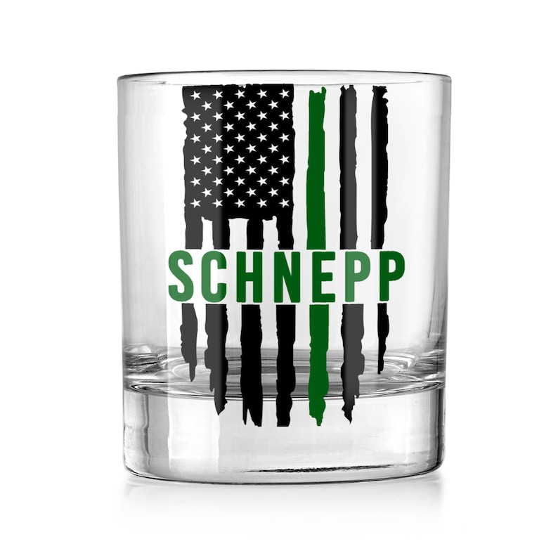May include: A clear glass tumbler with a black and green American flag design. The flag has a thin green line down the center. The name "SCHNEPP" is printed in green below the flag.