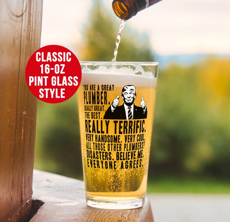May include: A 16-ounce pint glass with a black and white image of a man with a thumbs up gesture. The text on the glass reads "You are a great plumber. Really great. The best. Really terrific. Very handsome. Very cool. All those other plumbers? Disasters. Believe me. Everyone agrees."