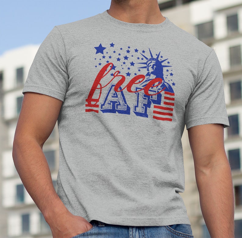 Peut inclure: Un t-shirt gris avec un motif d&eacute;lav&eacute; de la Statue de la Libert&eacute; et le texte "free AF" en bleu et rouge. Le motif est entour&eacute; d'&eacute;toiles blanches sur un fond bleu.