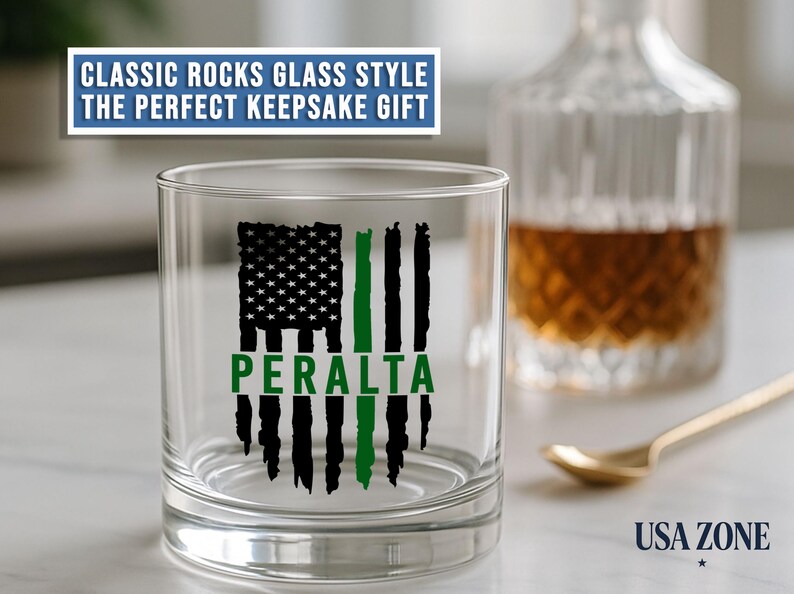 May include: A clear rocks glass featuring a black and green distressed American flag graphic with the name PERALTA printed in green across the center. The text CLASSIC ROCKS GLASS STYLE THE PERFECT KEEPSAKE GIFT appears above the glass.