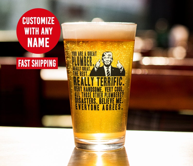 May include: A clear glass beer mug with a black and white graphic of a man with a thumbs up gesture. The text on the mug reads "You are a great plumber. Really great. The best. Really terrific. Very handsome. Very cool. All those other plumbers? Disasters. Believe me. Everyone agrees."