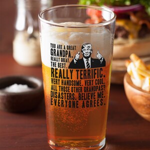 May include: A clear glass beer mug with a humorous message about a grandpa. The message reads "You are a great grandpa. Really great. The best. Really terrific. Very handsome. Very cool. All those other grandpas? Disasters. Believe me. Everyone agrees."